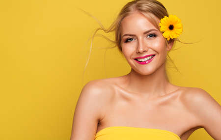 Happy Beauty Model Girl over Yellow Background. Cheerful Smiling Young Woman Freckles Face Portrait with Flower. Summer Cosmetic Skin Sun Care and Make upの写真素材