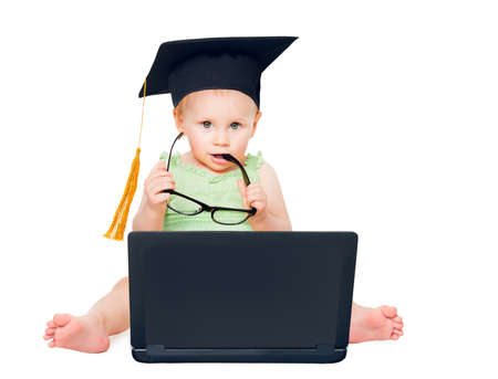 Funny Intelligent Child in Graduation Hat with Computer holding Eyeglasses. Curious Baby using Black Notebook looking at Camera. Little Kids Education Concept. Toddler sitting over White Studio Backgroundの写真素材