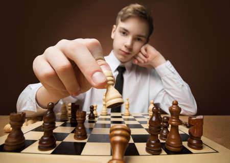 Checkmate. Chess Player Victory holding Chess Piece and throw off opposite King. Teenager Boy Leader win in Strategy Game. Studio Dark Backgroundの写真素材