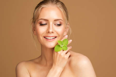 Smiling Beauty Model Smooth Skin with Mint. Woman Face and Body Health Care. Blond Girl with Wet Hair Holding Fresh Green Leaves over Brownの写真素材
