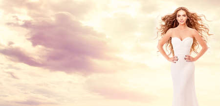 Red Hair Bride in White Dress over Sky Sunset. Beauty Model with Long Curly Hairstyle Art Portrait. Fantasy Red Head Woman over Sunny Sunshine Backgroundの写真素材
