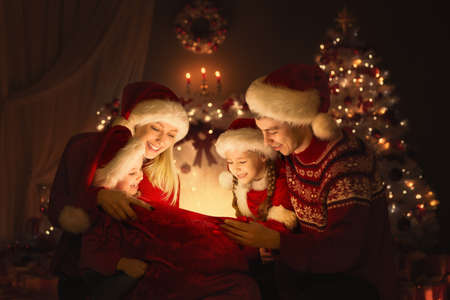 Christmas Family opening Santa Bag with Gifts. Happy Parents and Kids sitting in front of Decorated Xmas Fir Tree and looking at Magic Light. Winter Holiday Eveの写真素材