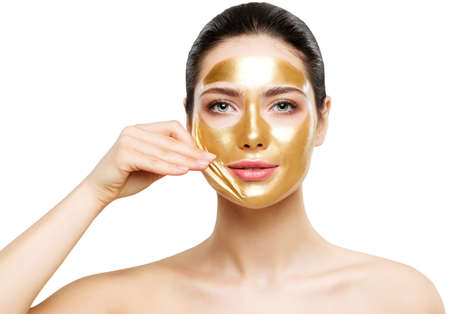 Woman Golden Peel off Face Mask. Beauty Model removing Gold Skin Mask over White Background. Facial Skin Care and Cosmeticsの写真素材