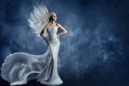 Winter Fashion Woman in Silver Sequin Dress. Beauty Model in Long Sparkle Glittering Gown over Fantasy Blue Snowy Christmas Backgroundの写真素材