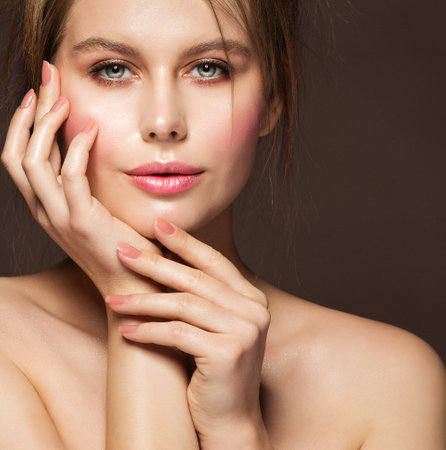 Face Beauty Woman. Model with Full Plump Glossy Lips and Smooth Skin holding Hands with Nude Nail Polish on Cheek over Dark Backgroundの写真素材