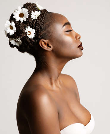 Beauty Profile of African American Woman with White Chamomile Flowers in Black Hair Braids. Fashion Portrait of Dark Skin Model over White. Wedding Make up and Bride Cornrows Hairstyleの写真素材