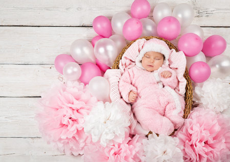 Newborn Girl sleeping in Pink Fluffy Bodysuit. Baby Birth Celebration with Balloons and Paper Flower Decoration. Cute Little Child Birthday. Dreaming Infant Portrait Top viewの写真素材
