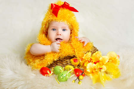Easter Baby. Newborn Child in Chicken Costume hatching out. Infant Kid in yellow Fuzzy Chick Hat sitting inside Basket with Easter Eggs. Birthday Holiday concept.の写真素材