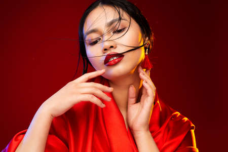 Asian Beauty Model with Red Lipstick Make up. Fashion Chinese Woman Portrait over Red Background. Face Skin Care and Salon Spa Cosmetology. Beautiful Girl massaging Neck and touching Chinの写真素材
