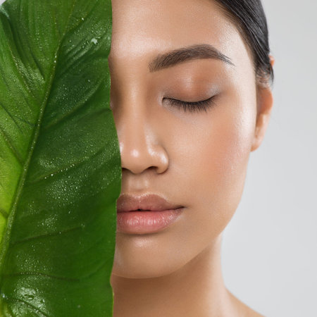 Skin Care. Natural Beauty Woman. Model with Fresh Clean Skin Make up and Full Lips with Big Green Tropic Leaf. Eco Cosmetics and Spa Cosmetology. Asian Girl Close up Portrait with Closed Eyesの写真素材