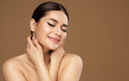 Skin Care. Beauty Face. Happy Woman enjoying Facelift Spa Massage. Model with Closed Eyes touching Fresh Clean Skin. Women Facial Cosmetology and Natural Makeup Cosmetics over beige backgroundの写真素材
