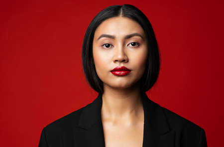 Asian Fashion Model. Woman Face with Red Lipstick Makeup. Elegant Lady Portrait over Red Studio backgroundの写真素材