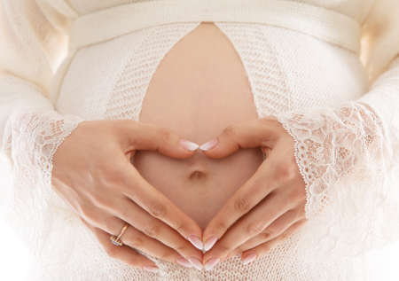 Pregnant Woman Belly with Heart shaped Hands. Maternity Health and Skin Care. Healthy Pregnancy and Childbirth. Mother Love Expectation Concept to Baby Embryoの写真素材