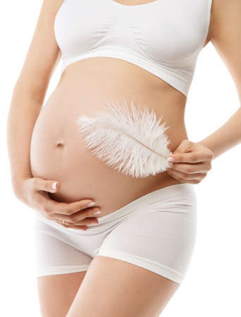 Pregnant Woman Belly Skin Care. Future Mother in White Cotton Underwear embrace Abdomen and massage with Feather. Pregnancy Healthy Cosmetics. Maternity Fit Body Beauty Concept over isolated Backgroundの写真素材
