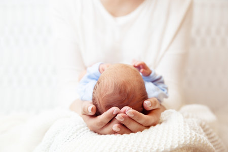Baby Head in Mother Hands. Mum holding Newborn Boy lying on White Blanket. Infant Health Care and Development. Child Birth and Parents Loveの写真素材