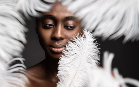 Black Woman Face with White Feather. Afro Beauty Model Face Skin Care and Cosmetics. Dark Skinned Women Fashion Portrait over Gray backgroundの写真素材