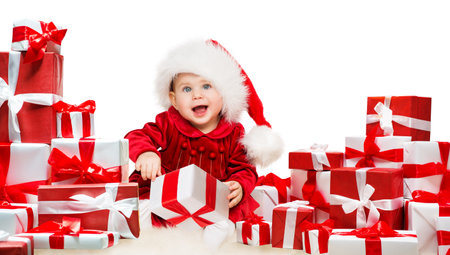 Christmas Baby with Gift Boxes. Happy Child in Santa Hat next to Stack of Xmas Presents with Red Ribbon Bow over White Background. Little Kid shopping. New Year Gifts Preparation and Deliveryの写真素材
