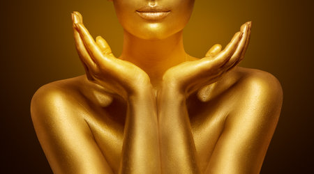 Golden Skin Woman Beauty. Gold Facial Mask and Lips Care Cosmetics Make up. Model Face Close up with open Hands under Chin over dark background. Female Luxury Spa Cosmetologyの写真素材