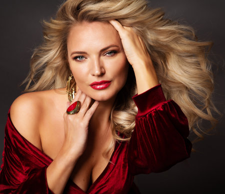 Woman Beauty Face Portrait with Blond Wavy Hair and Red Lips Makeup. Fashion Model with Luxury Curly Hairstyle and Gloss Make up closeup. Female Anti aging Facial Skin Care Cosmetics over Black Backgroundの写真素材