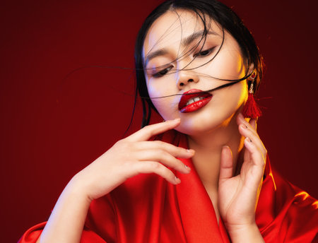 Beautiful Japanese Girl Face with Red Lips Makeup. Asian Beauty Woman in Red Silk Kimono Dress. Chinese Fashion Model. Fantasy Geisha Portraitの写真素材