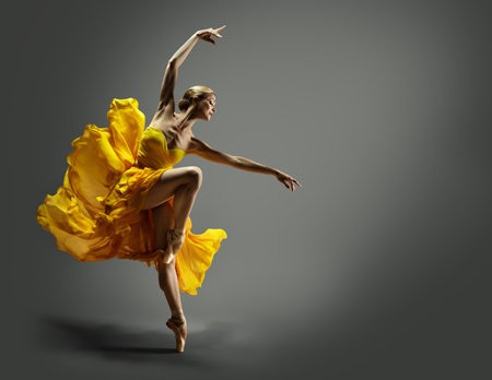 Ballerina in Yellow Chiffon Dress dancing over Gray Background. Ballet Dancer jumping in Air in Silk Gown. Modern Dance Graceful Woman performing in flying Skirtの写真素材