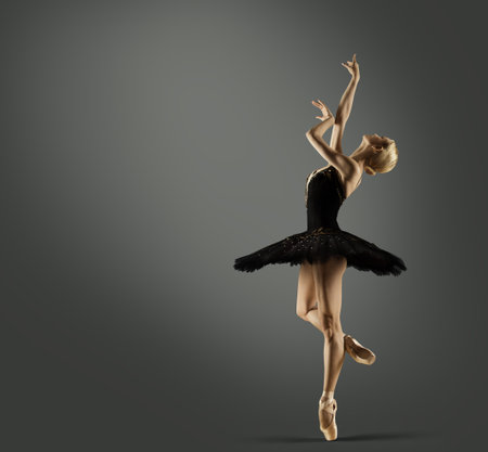 Ballerina in Black Tutu Skirt over Gray Studio Background. Ballet Dancer Silhouette in Swan Dress Balancing on Leg Pointe Shoes. Woman Dancing on Stageの写真素材