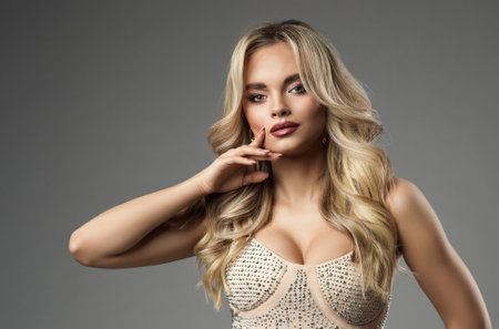 Beautiful Girl with Blond Wavy Hairstyle and perfect Lips Make up. Fashion Woman Portrait with beige Nails and smooth Blondie Hair. Beauty Model holding Finger on Chin over Grayの写真素材