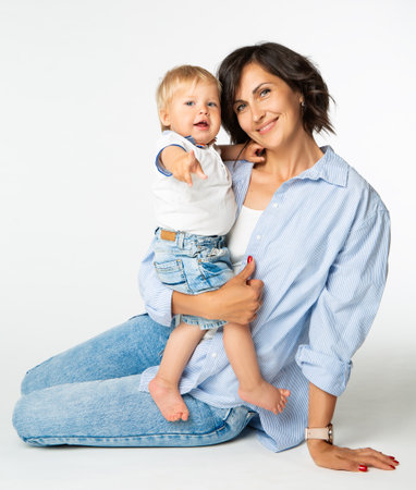 Happy Mother embracing smiling Baby. Adorable Infant Boy pointing Finger. Little Child playing with Mommy over White Background. Mom with one year Sonの写真素材