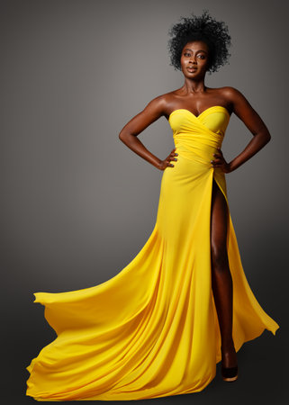 Fashion Dark Skin Woman in Yellow Silk Dress flying over Gray. African Model with Afro Curly Hair Style in Long Evening Gown. Stylish Lady Portraitの写真素材
