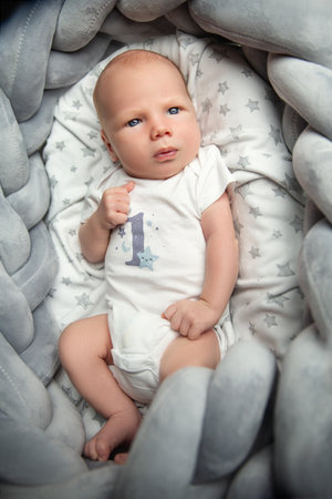 Newborn Baby Portrait looking at camera lying down on back in Gray Basket. One month little Child in White Bodysuit. Infant Clothing and Developmentの写真素材