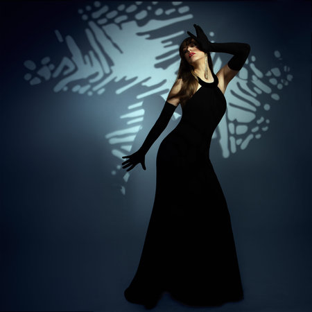 Mysterious Woman in long Black Dress perform on Art Stage. Lady in evening Gown over Shadow...