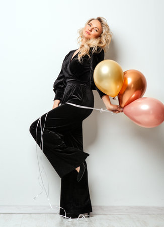 Beautiful Woman with Balloons over White background. Birthday Party Time. Fashion Model with Curly Hairstyle in Black Long Dressの写真素材
