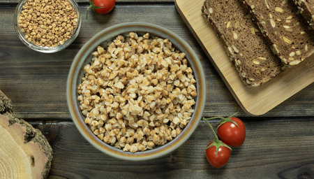 Buckwheat porridge in a plate on a wooden background on the table with cherry tomatoes and rye...
