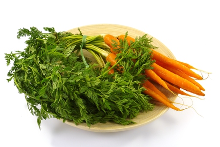 Fresh orange carrots with a green foliage on a bamboo plate over whiteの写真素材