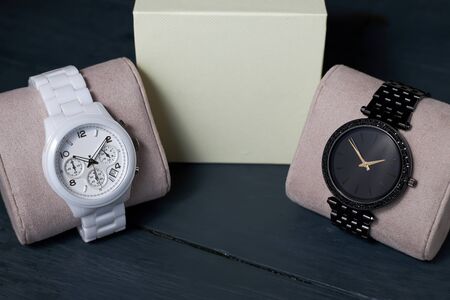 White ceramic and black steel wristwatches on the pillows and beige box on a wooden background.の写真素材