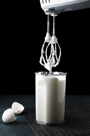 Beating a meringue with a mixer in a plastic beaker. White cream of egg whites for the cake. Black...