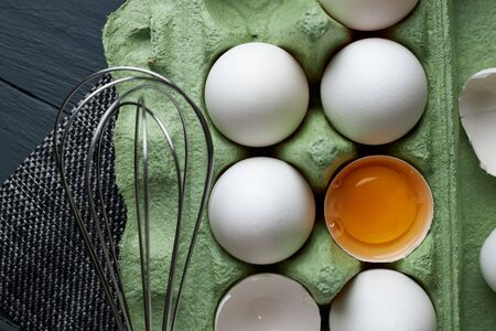 Group of raw white chicken eggs in green paper tray on wooden table, fresh half cracked egg and stainless steel egg whisk. Concept of healthy lifestyle.の写真素材