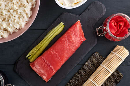 Pink salmon on a stone serving board with cucumbers, philadelphia cheese, dyed ginger, nori leaf and freshly cooked rice. Ingredients for making sushi rolls.の写真素材