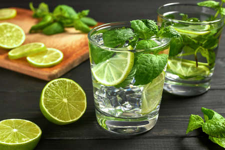 Two glasses of lemonade or mojito cocktail with ice, fresh mint and lime. Cold refreshing cocktail on black table.の写真素材