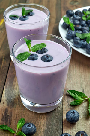 blueberry yogurt with fresh berries and mint leaves and a plate of blueberries on a wooden tableの写真素材