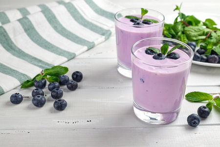 Blueberry yogurt served with fresh blueberries and mint leaves. Two glasses of yogurt on a white wooden table. Healthy breakfast.の写真素材