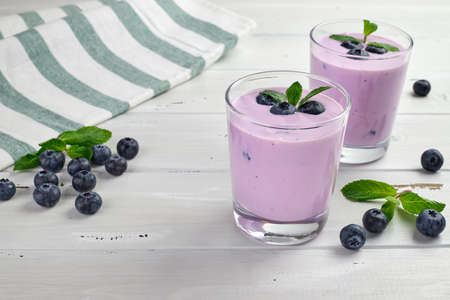 Blueberry yogurt served with fresh blueberries and mint leaves. Two glasses of yogurt on a white wooden table. Healthy breakfast.の写真素材
