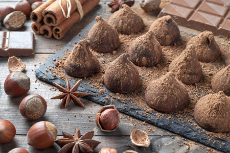 Homemade chocolate truffles sprinkled with cocoa powder and assorted chocolate with nuts and other spices on rustic old kitchen table.の写真素材