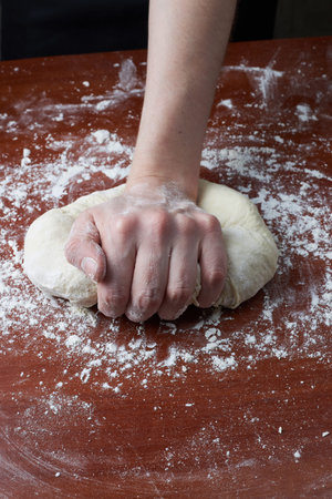 The woman kneads the dough with her hands. Female hands and raw dough on a wooden background. Pizza...