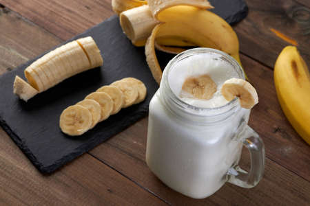 glass of tasty banana smoothie with sliced bananas on a wooden tableの写真素材