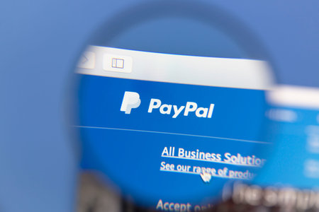 PayPal homepage under a magnifying glass. PayPal is an online payments system