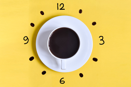 A cup of coffee on a yellow background (table) with watch face at 6 am (6 pm). Time to drink coffee. With coffee beansの写真素材