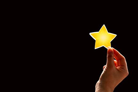 A woman gives a star. The concept of a positive rating, reviews and feedback on black background.の写真素材