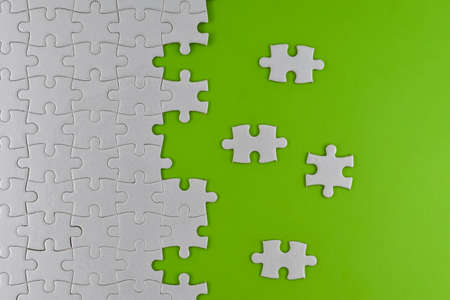 Unfinished white puzzle pieces on a green backgroundの写真素材