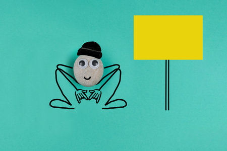 Animated pebble in a black wool cap squatting down, with big memo on blue paper backgroundの写真素材